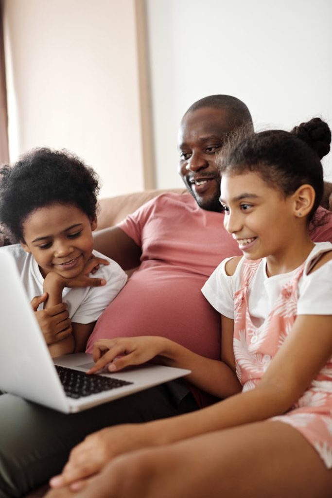 happy-family-sitting-and-looking-at-a-laptop-4260753 Smiling father and kids using a laptop at home, sharing joyful moments.